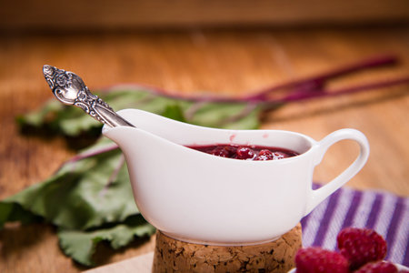 fresh ripe raspberry in white cup with jam on wooden background