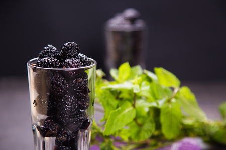 black juicy raw ripe mulberry in transparent glass on violet textileの写真素材