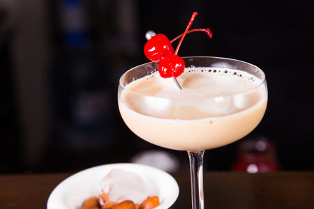 creamy alcoholic cocktail in transparent glass with cherry and nuts