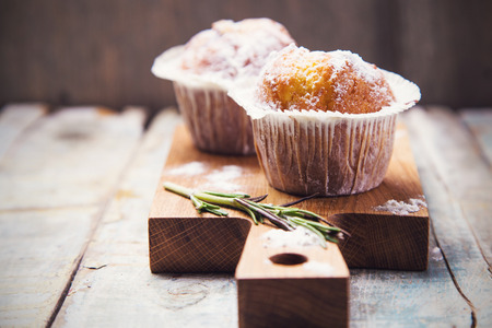 two fresh muffins in white flour on wooden plate in studioの写真素材