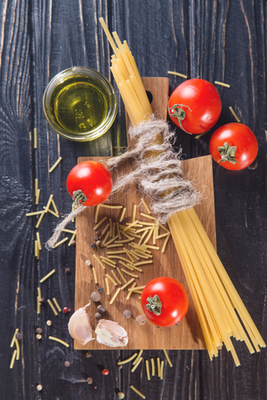 raw spaghetti with tomatoes and oil on black in studioの写真素材