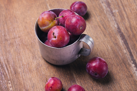 fresh wet red ripe raw plums in metallic old cupの写真素材