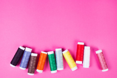 several spools of multicolored threads on a pink background in the studio