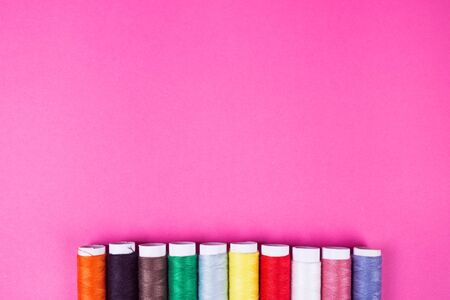 several spools of multicolored threads on a pink background in the studioの写真素材