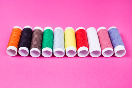 several spools of multicolored threads on a pink background in the studio