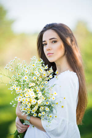 portrait of a beautiful young girl with bouquet, outdoors, in the fieldの写真素材