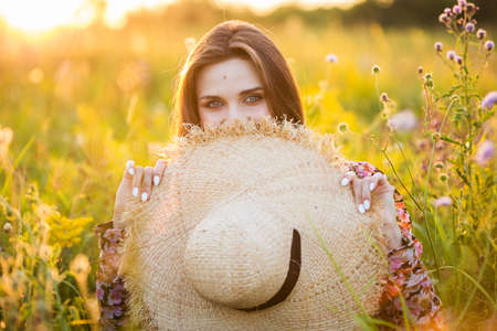 young beautiful european girl in the setting sun, on the field, in hatの写真素材