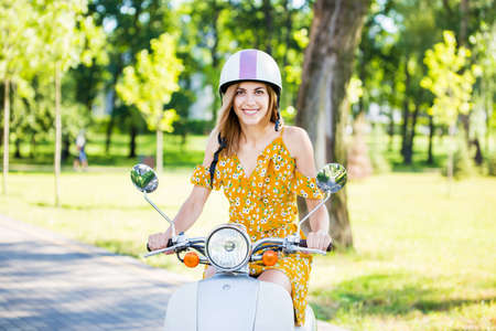 beautiful european girl in a yellow dress with a retro scooter in the morning parkの写真素材