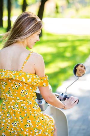 beautiful european girl in a yellow dress with a retro scooter in the morning parkの写真素材