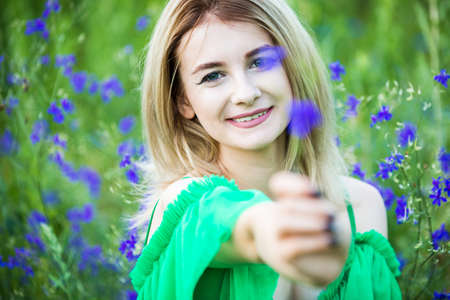 blond european girl in a green dress on nature with blue flowersの写真素材