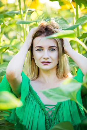 blond european girl in a green dress on nature with sunflowersの写真素材
