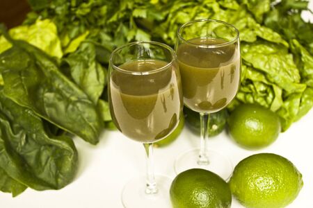 A couple of glasses of green juice with all kind of greeneries around.の写真素材