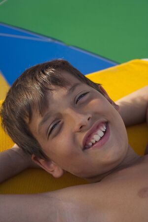 Child resting for a while under a colorful parasol in the beach.の写真素材