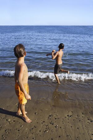 Boys throwing pebbles into the sea water.の写真素材
