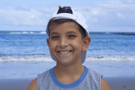 Child with a white cap smiling to the camera at the beach.の写真素材