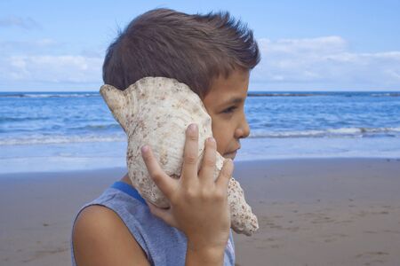 Kid listening the noise of the sea with the conch.の写真素材