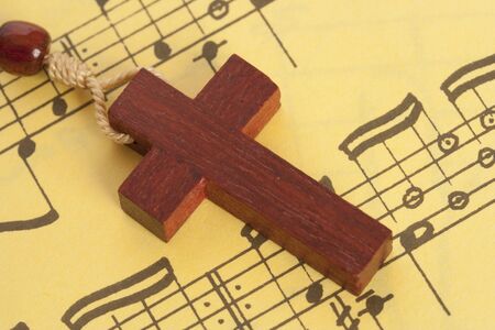 Small wooden cross over a yellow sheet  of religious music.の写真素材