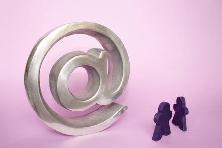 Two small figures in front of a symbol on pink background.の写真素材