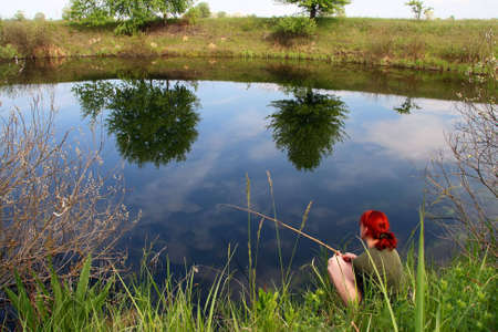 fishing on the small lake at spring, trees reflected in the calm waterの写真素材