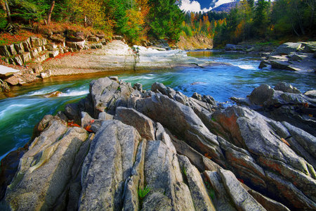 Mountain fast flowing river stream of water in the rocks with blue sky at autumn time. Colorfull...