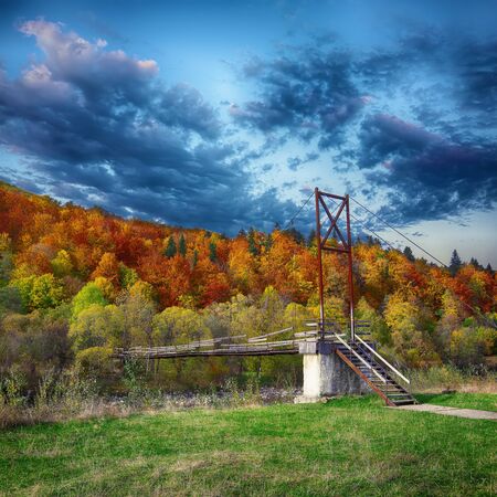 Wooden bridge over mountain river. Dramatic dark sky. Autumn timeの写真素材