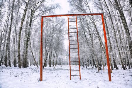 Snow-covered trees in the city park and old red horizontal bar with stairs. Wintert timeの写真素材