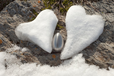Two Valentine's Day Hearts formed from snow and steel egg on rock surface.の写真素材