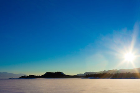 Sun and blue sky over frozen lake.