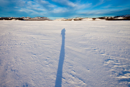 Long mid-winter shadow of person hiking through snowy landscape.の写真素材