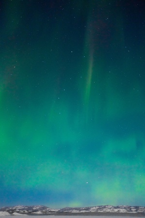 Northern Lights (Aurora borealis) over moon lit snowscape of frozen lake and forested hills.の写真素材