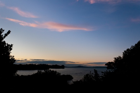 Orange sunset clouds in blue sky over dark coastal landscapeの写真素材