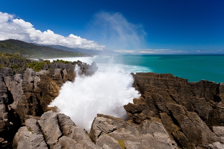 Surf of Tasman Sea crash into pancake rocks at Punakaiki, South Island, New Zealand, pushing saltwater spray out of blowholes high into the blue sky.の写真素材