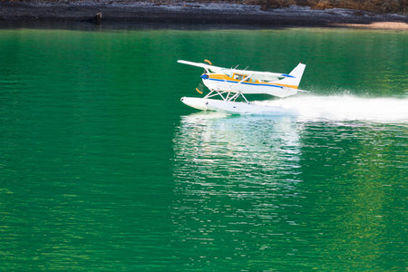 Small propeller float-plane or hydroplane takes off across flat calm water of lake