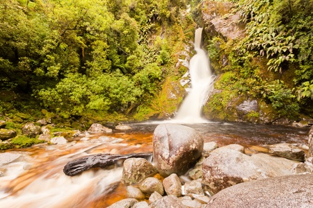 Forest waterfall cascading down rocky slope creating a refreshing pool surrounded by lush greenの写真素材