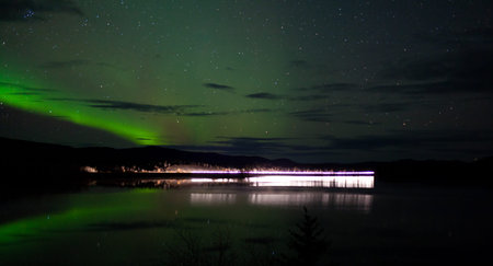 Night Sky Stars, clouds and Northern Lights over country road at lake shore, Yukon, Territory,...