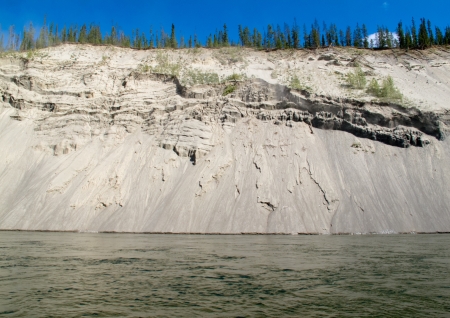 High cut bank of silt, sand and gravel slowly eroding by flowing water of mighty Yukon River, Yukon Territory, Canadaの写真素材