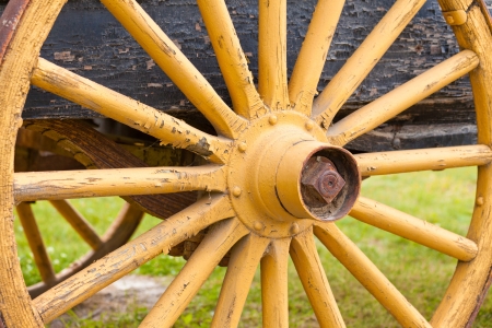 Old painted yellow wooden wagon wheel with spokes radiating from the hub on the axle of old cartの写真素材