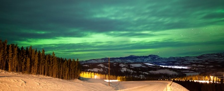 Northern Lights or Aurora borealis or polar lights illuminating overcast sky over snowy winter road landscapeの写真素材