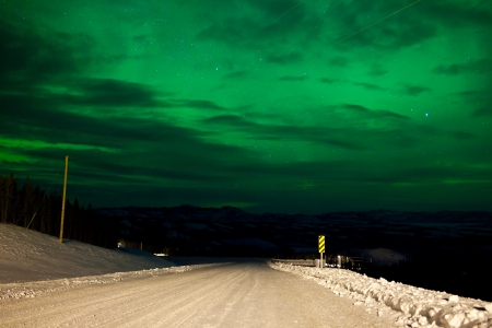 Northern Lights or Aurora borealis or polar lights illuminating overcast sky over snowy winter road landscapeの写真素材