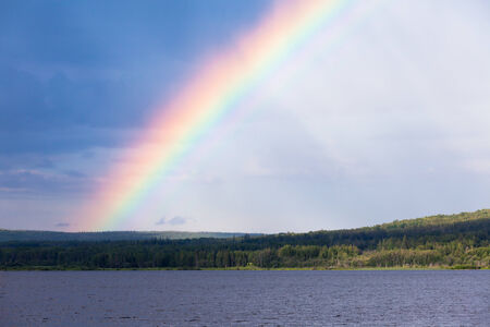 Intense Rainbow over surface of northern boreal forest taiga lake, northern British Columbia, Canadaの写真素材