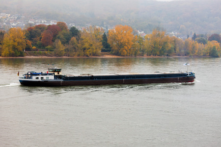 Bulk-carrier barge on waterway river Rhine with autumn fall colored landscape on shore, North Rhine-Westphalia, Germany, Europeの写真素材