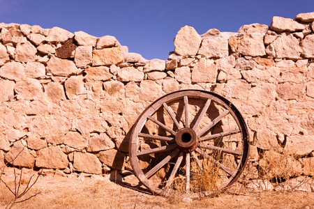 Historic wooden wagon wheel leaning against broken wall of natural stones as a relic of Wild West history in western Texas, USAの写真素材