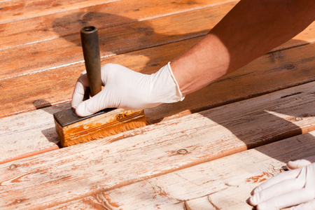 Painter staining deck boards with transparent protective outdoor decking paint applying stain with brush with special attention to the gapsの写真素材