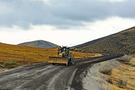 Grader road maintenance heavy equipment on gravel dirt road of remote Dempster Highway in arctic tundra landscape of northern Yukon Territory, YT, Canadaの写真素材