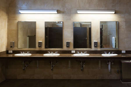 Simple efficiency of clean tiled modern interior public washroom with multiple sinks, faucets, soap dispensers and mirrorsの写真素材