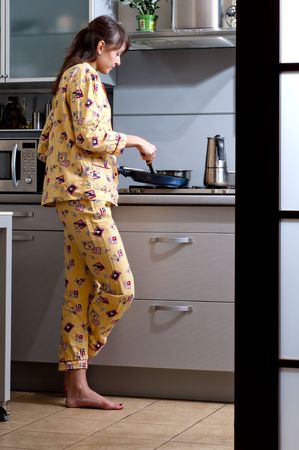 Beautiful young woman is cooking breakfast. She is dressed in sleepwear.の写真素材
