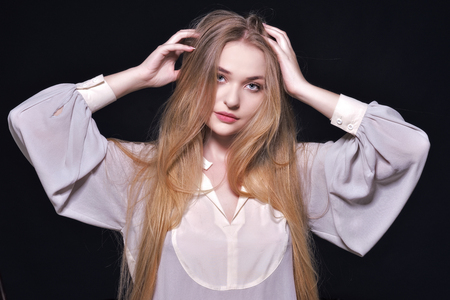 Portrait of the undressed beautiful woman with long blowing hair in white blouse. Studio shooting with dark background. Natural make-up.の写真素材