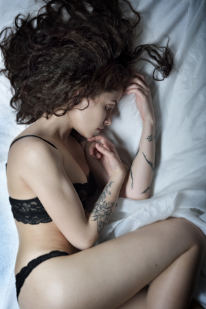 Beautiful woman with tattoo in  lace black  underwear laying on the bed. Studio shooting. Veiw from top angleの写真素材