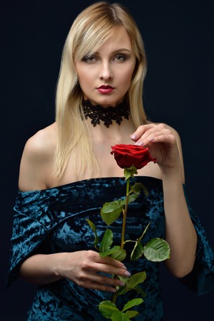 Portrait of the Beautiful blonde woman in velvet dress with red rose. Shooting in studio with dark background.の写真素材