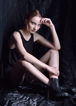 Sitting beautiful woman in black top and shoes  in studio with dark background.の写真素材